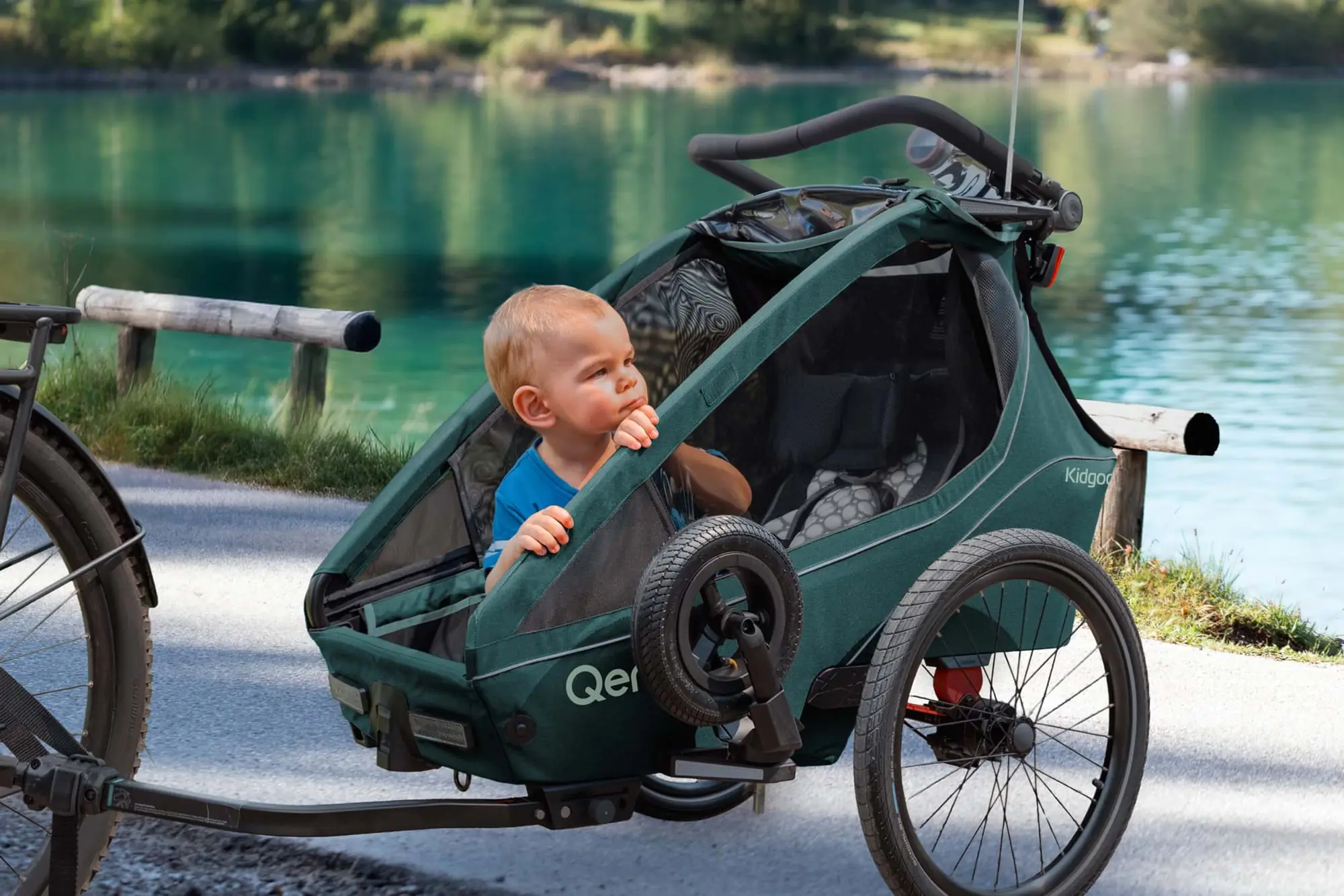 Kleinkind schaut aus einem Kidgoo 1 in Pacific Blue, der an einem See am Fahrrad hängt